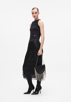 Black sleeveless top with a metallic accent, paired with a black fringed sequin skirt. The model holds a black handbag with silver fringe.