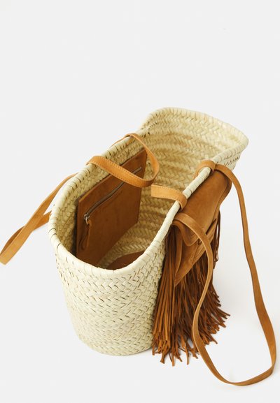 Sac fourre-tout en paille tissée avec une poche en cuir tan à franges attachée et des poignées en cuir assorties, présenté sur fond blanc.