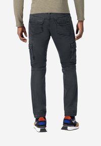 Zwarte cargobroek met meerdere zakken, taps toelopend ontwerp van de pijpen en een zachte, gestructureerde stof. Gecombineerd met meerkleurige sportschoenen.