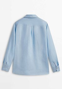 Chemise bleu clair à manches longues vue de dos, avec un pli central au dos et des poignets boutonnés.