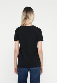 Zwarte katoenen t-shirt met korte mouwen en een ronde halslijn, vanachter gezien. De stof lijkt glad met een aansluitende snit.
