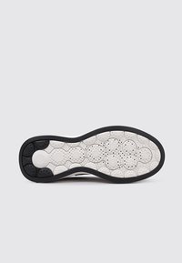 Suela de zapato con un borde exterior negro y una media suela de goma blanca. Diseños circulares texturizados y agujeros de ventilación mejoran el agarre y la flexibilidad.