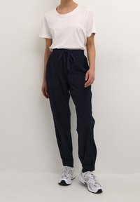 Vit bomullströja med korta ärmar, i kombination med mörkblå byxor med elastisk midja och två framfickor. Sneakers ingår.