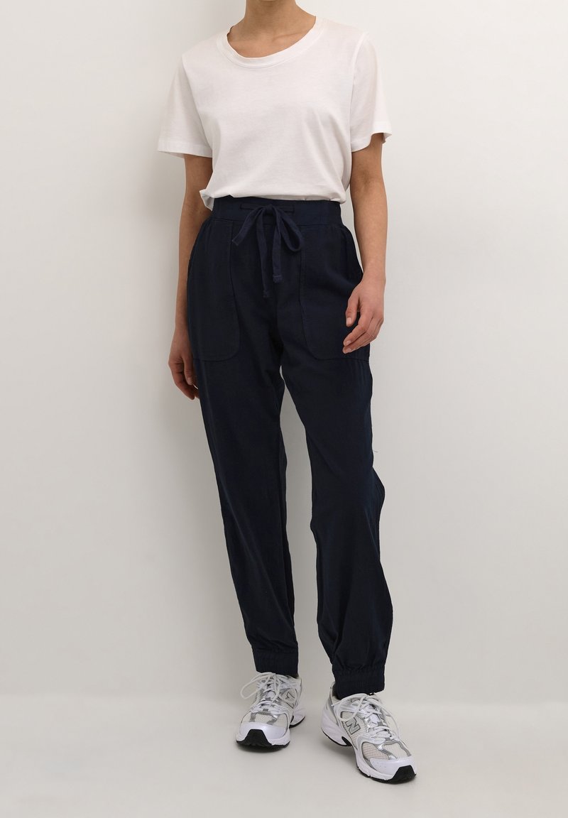 Vit bomullströja med korta ärmar, i kombination med mörkblå byxor med elastisk midja och två framfickor. Sneakers ingår.