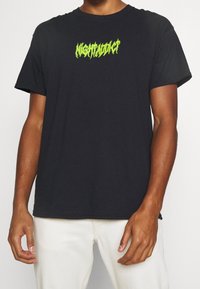 Black cotton T-shirt featuring a textured neon green graphic text "NIGHTADDICT" centered on the chest, with a relaxed fit and crew neck.