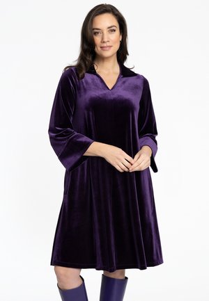 Lila Samtkleid mit V-Ausschnitt und Dreiviertelärmeln, das einen lässigen Schnitt und Taschen bietet. Glatte Textur und fließende Silhouette.