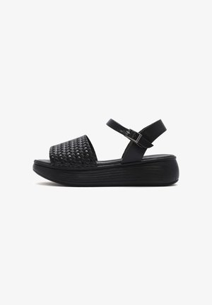 Black platform sandals with a woven texture on the upper, adjustable buckle strap, and a ridged, contoured sole.