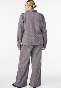 Sada s šedými puntíky obsahující volnější dlouhý rukáv s límcem a široké kalhoty, obojí vyrobené z měkké a hladké látky.