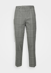 Pantalon à carreaux noirs et blancs présentant un large motif à carreaux, des jambes fuselées, des passants de ceinture et des poches latérales avec une finition texturée.
