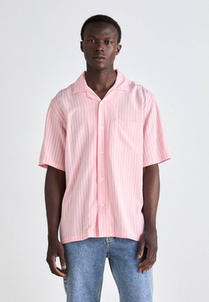 Kortermet rosa stripete skjorte i lett stoff med lomme. Har klassisk krage og hvite knapper, båret med blå jeans.