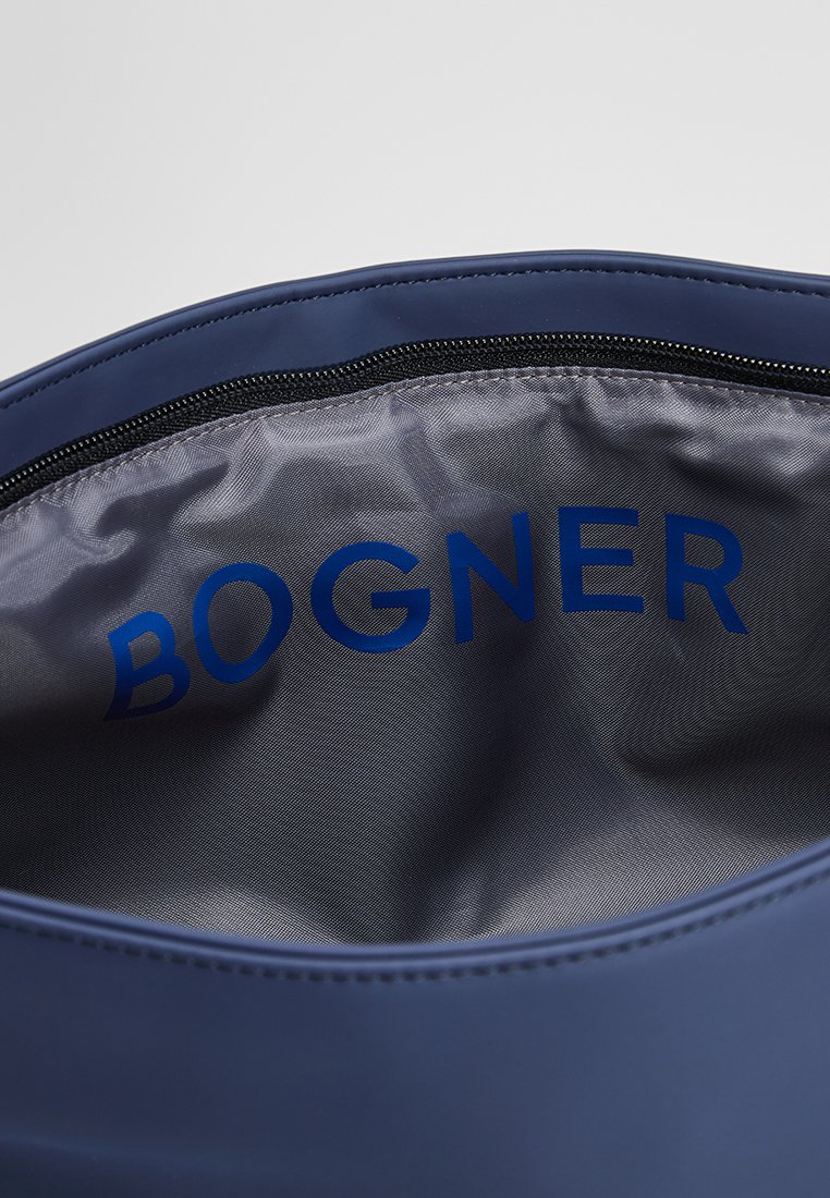 Zbliżenie wnętrza niebieskiej torby, pokazujące srebrną podszewkę z czarnym zamkiem błyskawicznym oraz nazwą marki "BOGNER" nadrukowaną wewnątrz.