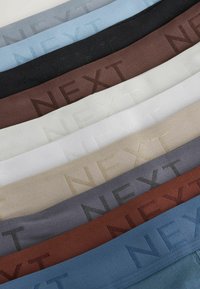 Colección de cintas de tela en varios colores, incluyendo azul, negro, marrón, gris y blanco, con la palabra "NEXT" grabada en un tono a juego.