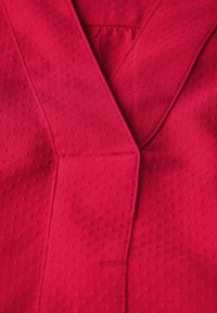 Tissu rouge au toucher lisse, présentant un design en V et de légères perforations pour la respirabilité. Inclut des détails de couture.
