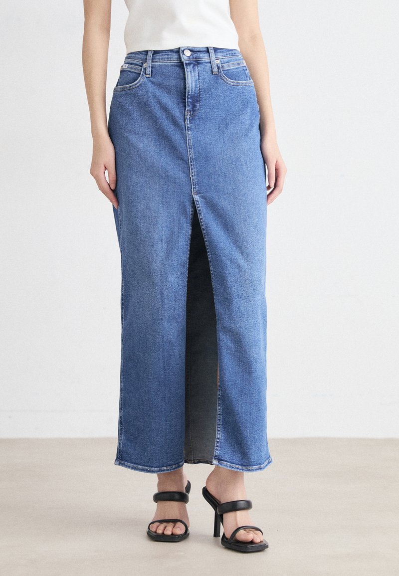 Denim maxiskjørt i mellomblått med frontspalte, klassisk fem-lommers design og synlige sømdetaljer. Kombinert med svarte hælsandaler.