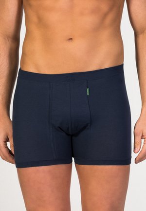 Boxer shorts de color azul marino hechos de una tela suave. Cuentan con un bolsillo frontal y un logotipo cerca de la cintura, con un diseño ajustado.