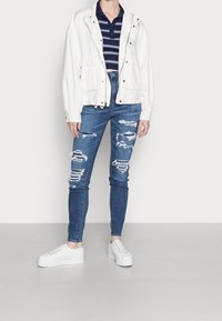 Vit zip-up jacka, marinblå randig polo skjorta, slitna blå skinny jeans och vita plattformssneakers. Funktioner inkluderar synliga rivningar och fickor.