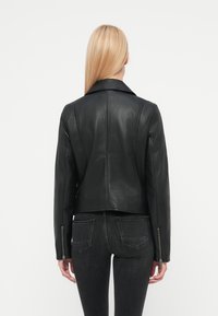 Μαύρο δερμάτινο μπουφάν με γιακά σάλι, εφαρμοστή γραμμή και φερμουάρ στα μανίκια. Ομαλή υφή και αδιάκοπη πίσω όψη. Συνδυασμένο με σκούρο τζιν.