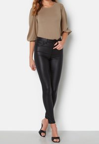 Beige topp med puffärmar som matchas med svarta leggings i konstläder. Leggingsen har hög midja och en slät, blank yta. Svarta öppna klackar.