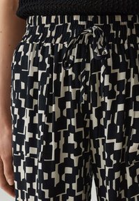 Zwart-wit gestreepte broek met een elastische tailleband, trekkoord en zijzakken, met een geometrisch ontwerp.