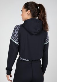 Geknipte zwarte hoodie met een capuchon, voorzien van grijze dierenprint mouwen en witte logo-details. Zachte stof met een aansluitende snit.