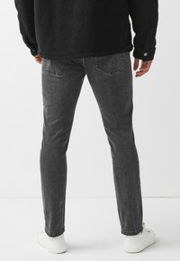 Tmavě šedé džínové kalhoty slim fit, s zadními kapsami a mírně vybledlou texturou. V kombinaci s bílými teniskami.