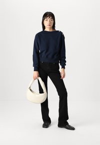 Navy blue sweatshirt with gold buttons on the shoulder, paired with black jeans and a white hobo bag. The fabric appears soft and textured.