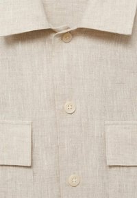 Bežna lanena srajca z nazobčanim ovratnikom, dvema žepoma in lahkim, teksturiranim materialom. Gumbi so okrogli in svetlih barv.