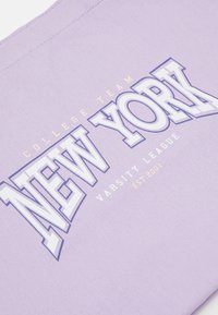 Tissu violet avec texte souligné en blanc et bleu indiquant "NEW YORK", texte plus petit "COLLEGE TEAM", "VARSITY LEAGUE" et "EST 2001."