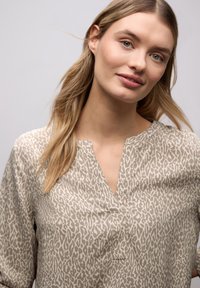 Blouse légère taupe avec un motif animalier. Dotée d'un col en V, de manches longues et d'une coupe décontractée. Texture lisse.