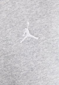 Silhouette blanche brodée d'un joueur de basketball sautant avec un ballon sur un fond de tissu gris clair.