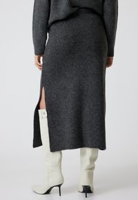 Jupe tricotée gris foncé avec une forte fente, texture douce et détails côtelés ; associée à des bottes blanches à talons pointus arrivant au genou.