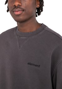 Dunkelgrauer Sweatshirt mit geripptem Halsausschnitt und dezentem schwarzem Logo. Besitzt einen lässigen Schnitt und strukturiertes Material mit sichtbaren Nähtelementen.