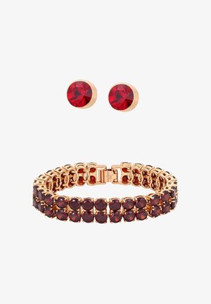 Aranyszínű ékszerszett, amely karkötőt tartalmaz piros kristályokkal és hozzáillő, bedugós fülbevalókat. Kapoccsal és kerek, csiszolt kövekkel díszített.