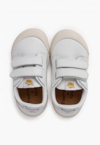 Zapatos de cuero blanco con dos correas de velcro, suelas de goma beige, textura suave y un pequeño logo amarillo en la lengüeta.
