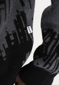 Gestrickter Pullover in Schwarz und Grau, mit einem geometrischen Muster und einem kleinen Etikett. Die Textur ist weich, mit gerippten Bündchen.