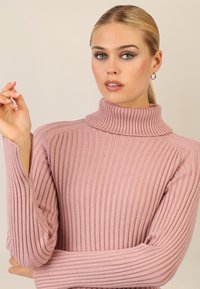Różowy sweter z golfem, z długimi rękawami, o dopasowanym kroju. Miękka struktura z wyraźnymi pionowymi liniami.