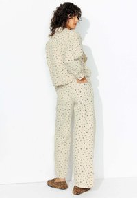 Ensemble en tissu beige à motifs avec des designs floraux. La chemise ample à manches longues et le pantalon large. Chaussons à imprimé animal marron.