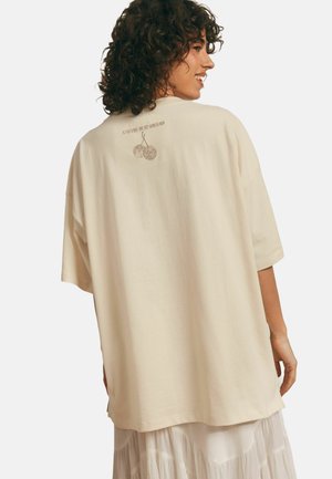 Kremowa, oversize t-shirt z krótkim rękawem, z nadrukiem z tyłu przedstawiającym wiśnie oraz napisem "A RYTM TRWA DALEJ" w subtelnej brązowej kolorystyce. Miękka w dotyku.