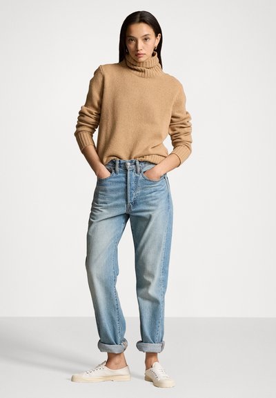 Beige gebreide coltrui, losse pasvorm, gecombineerd met lichtblauwe high-waisted denim jeans, omgeslagen bij de enkels, gedragen met beige canvas sneakers.