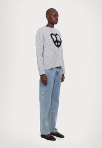 Γκρι πλεκτή μπλούζα με σχέδιο μαύρου συμβόλου ειρήνης, συνδυασμένη με ανοιχτό μπλε τζιν παντελόνι και μαύρες μπαλαρίνες. Υφή, άνετη εφαρμογή.