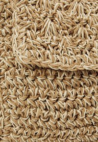 Detailní záběr na texturovanou tkanou podložku s tlustými pletenými vlákny ve střídajících se světle a tmavě béžových pramenech.