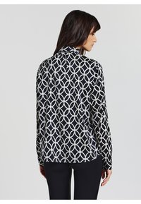 Langarmhemd mit schwarzem Hintergrund und einem weißen geometrischen Muster aus ineinandergreifenden Kreisen. Glattes Material mit einem vielseitigen Design.