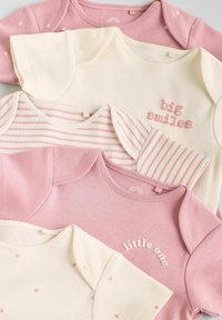 Collezione di magliette per bambini in rosa e crema. Le caratteristiche includono motivi a cuore, testi ricamati ("grandi sorrisi", "piccolo") e design a righe.