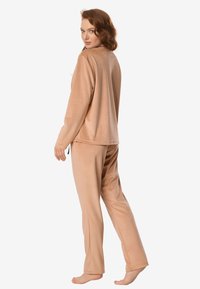 Beżowy zestaw do noszenia w domu wykonany z miękkiej tkaniny. Składa się z bluzki z długim rękawem oraz spodni o prostych nogawkach, o luźnym kroju i minimalistycznym designie.