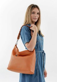 Borsa a mano in pelle arancione con finitura texturizzata, dotata di una tracolla intrecciata e hardware in tonalità argento. La forma è morbida con una silhouette afflosciata.