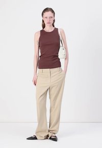 Bruine geribde tanktop, beige wijde broek, zwarte puntige ballerina's en een witte tas, tegen een plain witte achtergrond.