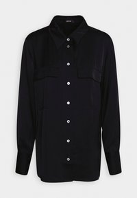 Camicia blu navy con bottoni, maniche lunghe, due tasche frontali e colletto classico. Presenta bottoni lucidi e una texture liscia.