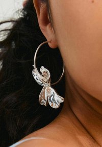 Silver hoop earring featuring a textured floral design. The floral accent resembles petals and is detailed with a smooth finish.