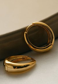 Orecchini a cerchio in oro con una finitura liscia e lucida, caratterizzati da un design arrotondato e una chiusura sicura. Presentati su uno sfondo neutro.
