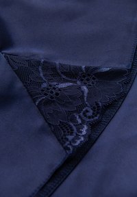 Mörkblå satin-tyg med en spetspanel med blommönster. Spetsen har intrikata detaljer och vågiga kanter längs sömmen.